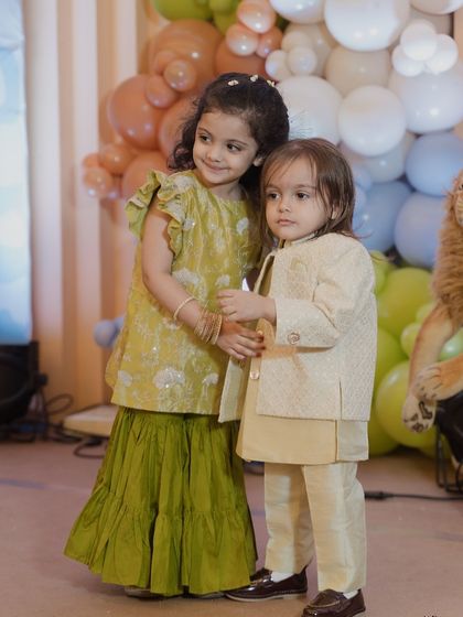 A sweet moment between siblings at the Mundan ceremony. The pastel jungle-themed backdrop adds a touch of modern whimsy to the traditional event.
