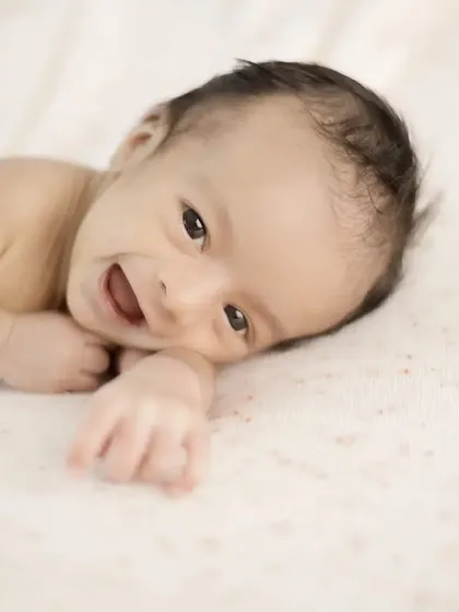 A heart-melting smile from a newborn during a simple tummy time pose. This shot captures a moment of pure, unfiltered joy on a soft, neutral blanket.