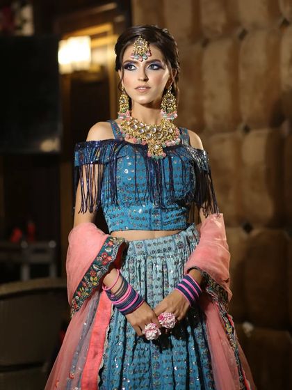 This blue lehenga with a cold-shoulder, fringed blouse is a super trendy option for a sangeet or mehendi. It's paired with beautiful floral jewelry.