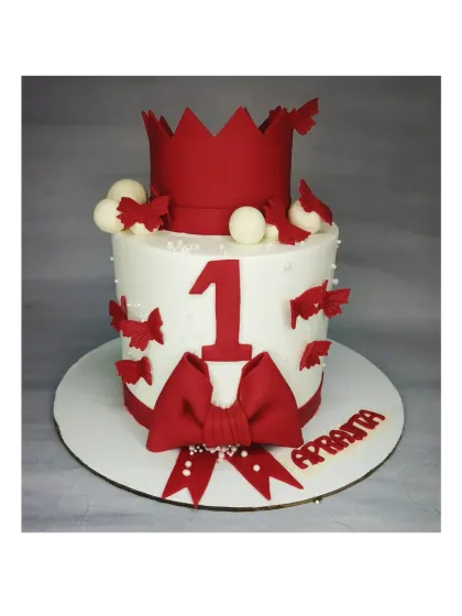 A bold and beautiful first birthday cake in red and white. This chocolate truffle Ferrero Rocher cake is decorated with a crown, a large bow, and butterflies.