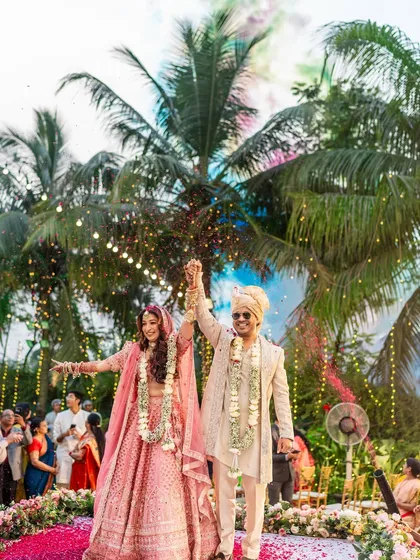 A triumphant moment post-varmala, with hands raised in celebration and colorful smoke bombs adding to the festive atmosphere.