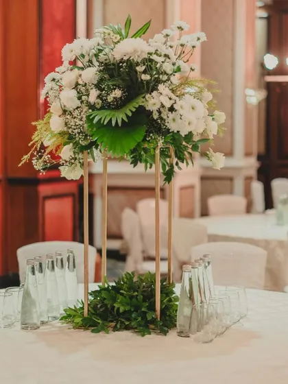 An elegant floral centerpiece for a reception table, using a tall, slender gold stand to elevate the arrangement without obstructing conversation.