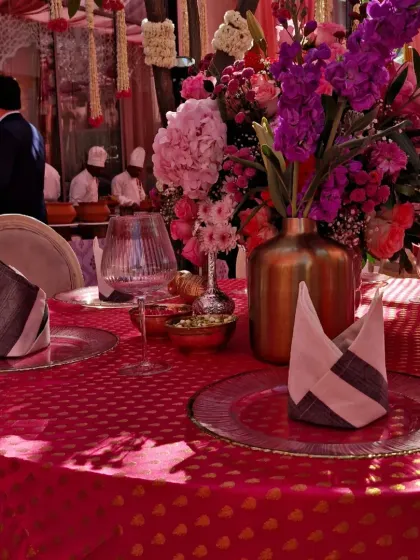 A close-up showing the play of light and shadow on the textured pink tablecloth, with the vibrant floral centerpiece and elegant tableware creating a beautiful composition.