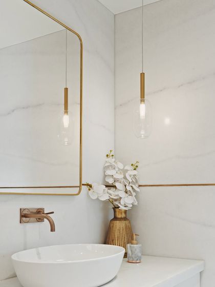 This bathroom in the Maximum City Duplex has a brighter, more glamorous feel, with white marble walls, brass inlays, and delicate glass pendant lights.