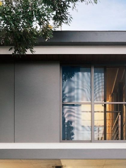 A close-up of the upper level's facade, showing the clean lines of the grey paneling and the large sliding glass door that opens onto a balcony.