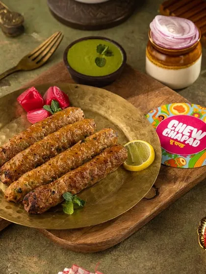 Juicy Seekh Kebabs fresh off the grill for Chew Chapad. The lighting highlights the smoky char and texture, while the mint and pickled onions suggest the fresh accompaniments that complete the dish.