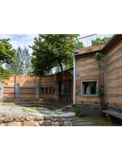 The building's exterior showcases a blend of natural materials. A stratified rammed earth wall sits beside a stone-lined courtyard, demonstrating how different textures and colors from the earth can create a harmonious facade.