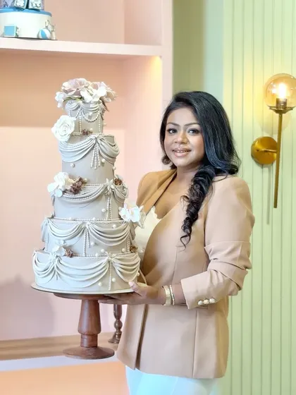 This is more than a cake; it's a canvas for your celebration. Here I am in our new studio with an elegant, multi-tiered wedding cake featuring intricate drapery and sugar flowers, a testament to the artistry we pour into every creation.