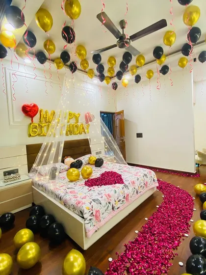 A surprise birthday room decoration designed for a romantic celebration. This service includes balloons on the ceiling, a 'Happy Birthday' foil balloon set, a pathway of fresh rose petals, and a heart shape on the bed.