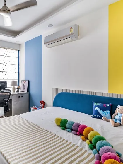 A vibrant and cheerful bedroom with bold color blocking in blue and yellow, a comfortable bed, and a dedicated study corner by the window.