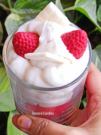 A dessert candle with whipped cream and strawberry toppings, held against a green background.