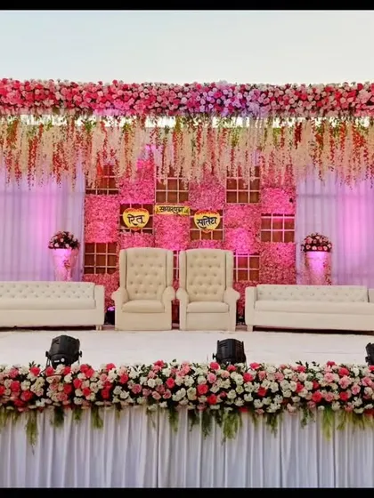 This reception stage is a vision in pink, featuring a ceiling of hanging floral strings and a dense flower border. The combination of plush white seating and warm pink lighting creates a romantic and luxurious atmosphere.