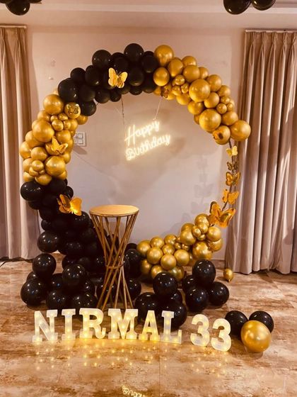 A chic 33rd birthday decoration using a black and gold balloon ring, butterfly accents, and marquee letters for the name.