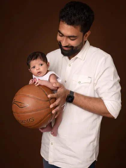 A father looks down lovingly at his one-month-old son, who is perched on a basketball. This unique portrait blends a personal passion with a classic studio style.
