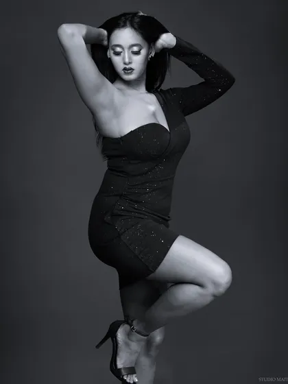 A dramatic monochrome portrait of a model in a one-shoulder dress. The lighting is sculpted to emphasize her pose and the texture of the fabric.