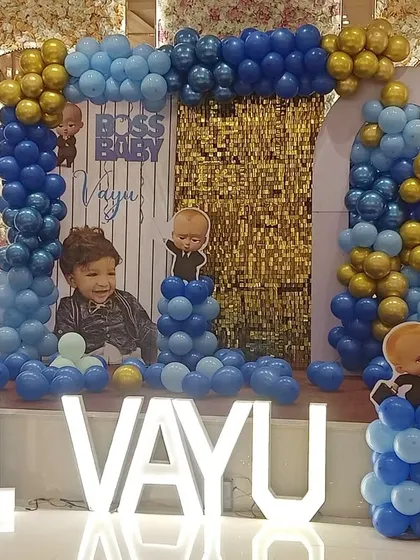 A wider shot of Vayu's first birthday setup, showing the Boss Baby themed stage with balloon pillars and character cutouts in a beautiful banquet hall.