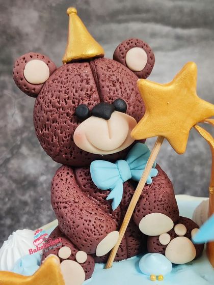 A close-up of the adorable, handcrafted fondant teddy bear topper, complete with a party hat and a magic star wand. Every detail is made with love for the little birthday boy.