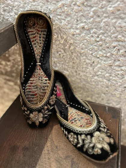 The right pair of juttis completes an outfit. This close-up reveals the detailed floral embroidery on rich black velvet, a perfect blend of traditional design and comfort.