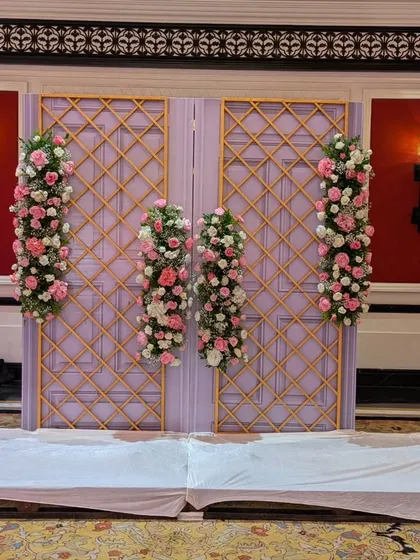 A simple yet elegant backdrop element, featuring lavender-colored doors with a golden lattice overlay, adorned with delicate pink and white floral arrangements.