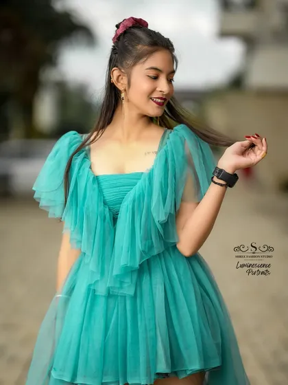 A candid and playful moment, with the model twirling a strand of hair, her teal dress adding a splash of color to the scene.