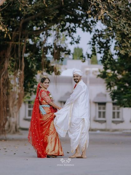 The couple holding hands, the bride in her vibrant red saree and the groom in his traditional white dhoti.