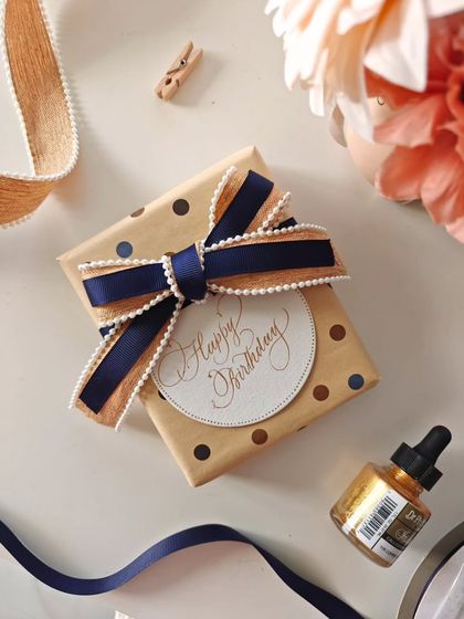 A birthday gift wrapped with a beautiful navy and gold ribbon, finished with a round, handwritten "Happy Birthday" tag. Personalization is the new definition of premium.
