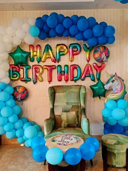 A colorful unicorn-themed birthday setup at home. We created a photo corner with a half-arch of blue and white balloons, rainbow "Happy Birthday" foil letters, and a cute unicorn balloon.