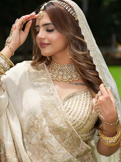 The epitome of grace. This ivory and gold ensemble features a stunning Kundan choker, matching matha patti, and a full set of bangles, creating a look of pure elegance for any grand celebration.