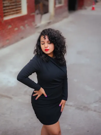 A full-body shot of the model in a black dress against a gritty, urban background. The composition emphasizes her confident stance and the mood of the location.
