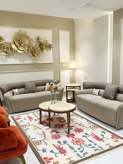 The living room of a South Mumbai residence, where I curated an earthy yet luxe palette. The space features comfortable taupe sofas, vibrant terracotta armchairs, and a stunning floral rug, all brought together by a dramatic metal wall sculpture.