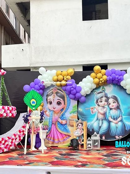 A grand outdoor stage setup for a Krishna-themed birthday. The decor includes a large floral moon prop, custom backdrops, and character cutouts.