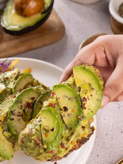 A close-up of a hand holding a slice of avocado toast. This perspective is personal and engaging, making the viewer feel like they are about to take a bite.
