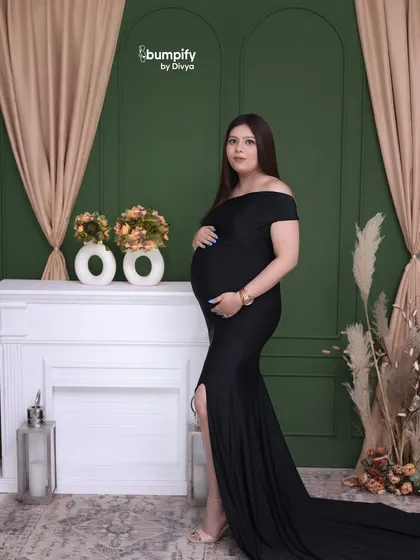 A classic and elegant studio portrait. The mom-to-be looks beautiful in a black gown against a deep green wall with a white fireplace mantle.