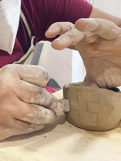 A student uses a stamp to add a repeating pattern to their pinch pot, combining simple form with intricate detail.