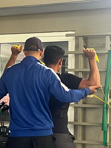 A physiotherapist guides an athlete through a resistance band exercise to strengthen the rotator cuff and prevent shoulder injuries, which are common in golf.