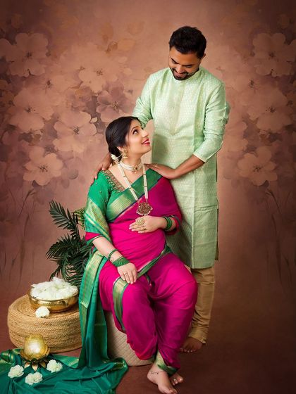A sweet moment between an expecting couple dressed in traditional Indian clothing. The warm, painterly backdrop complements the vibrant colors of the saree.