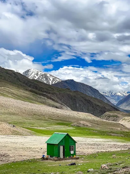 A small, green hut stands alone in a vast, barren landscape in Spiti Valley. This image highlights the solitude and immense scale of the Himalayan wilderness.