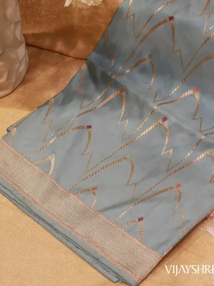 A soft-draping Banarasi Kathan silk saree in a beautiful grey-blue. The geometric zari weaving adds a modern touch to this traditional fabric, known for its fine texture and elegance.