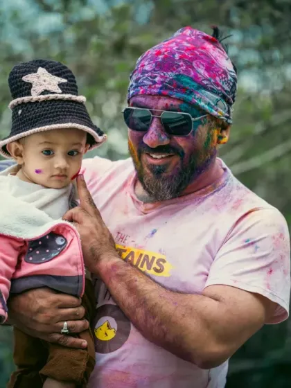 A father gently applies a spot of color to his son's cheek. This simple gesture, captured up close, is a beautiful symbol of this special milestone, the baby's first Holi.
