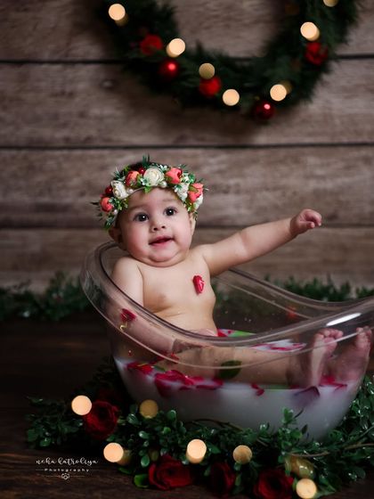 A festive milk bath session. The combination of the rustic wood background, a Christmas wreath, and a floral crown creates a unique and charming holiday-themed baby photo.