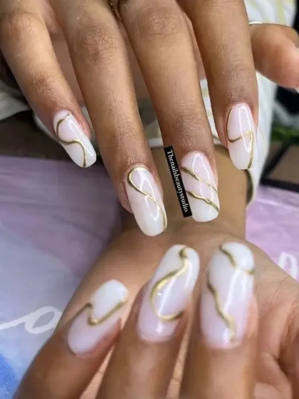 An elegant and classy design with milky white nails and delicate, hand-painted gold swirls.
