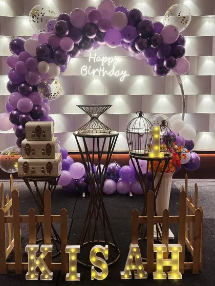 An elegant lavender and white themed decoration with a balloon arch, neon sign, and vintage-style props.