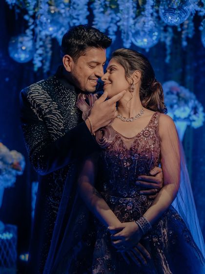 A tender moment during the Sangeet night, with the groom gently holding the bride's face. The blue lighting creates a romantic and dreamy mood.