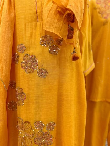 A close-up of the delicate, beaded floral embroidery on a yellow kurta, highlighting the fine craftsmanship.
