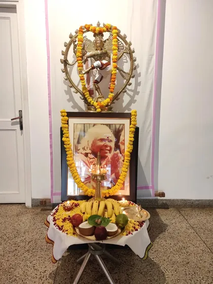 An altar setup for Swami Vishnudevananda's mahasamadhi day, with his portrait, a lamp, and offerings of fruit and flowers.