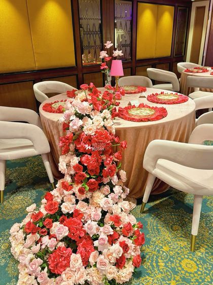 We use florals to create dramatic, flowing installations. Here, a cascade of red and pink roses flows from the tabletop to the floor, creating a stunning visual effect that is both opulent and artistic.