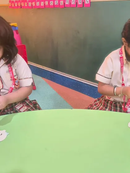 Two girls work on assembling their Grandparents Day cards, carefully gluing the pieces together.