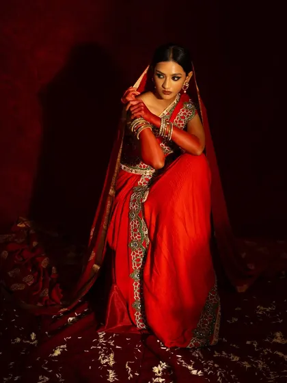 A different angle from the red bridal shoot, capturing a more vulnerable, seated pose. The scattered petals on the floor add texture and a sense of romance.