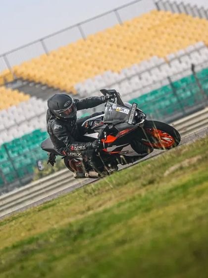 A rider on a KTM navigates a corner at BIC, with the Indian tricolor visible on the grandstand seats in the background.