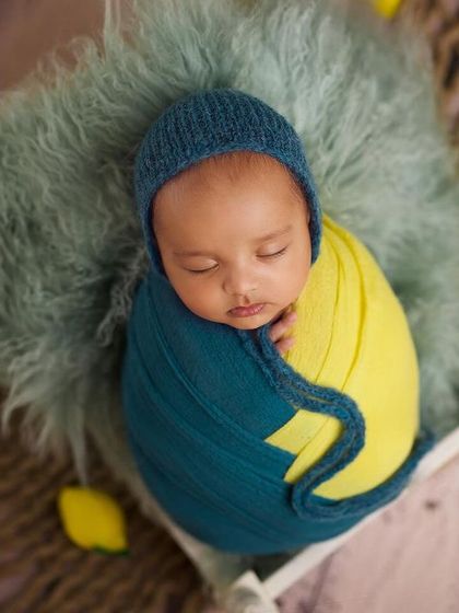 A newborn wrapped in yellow and teal, nestled in a basket with lemon props. This colorful and fresh theme is perfect for a unique baby announcement.
